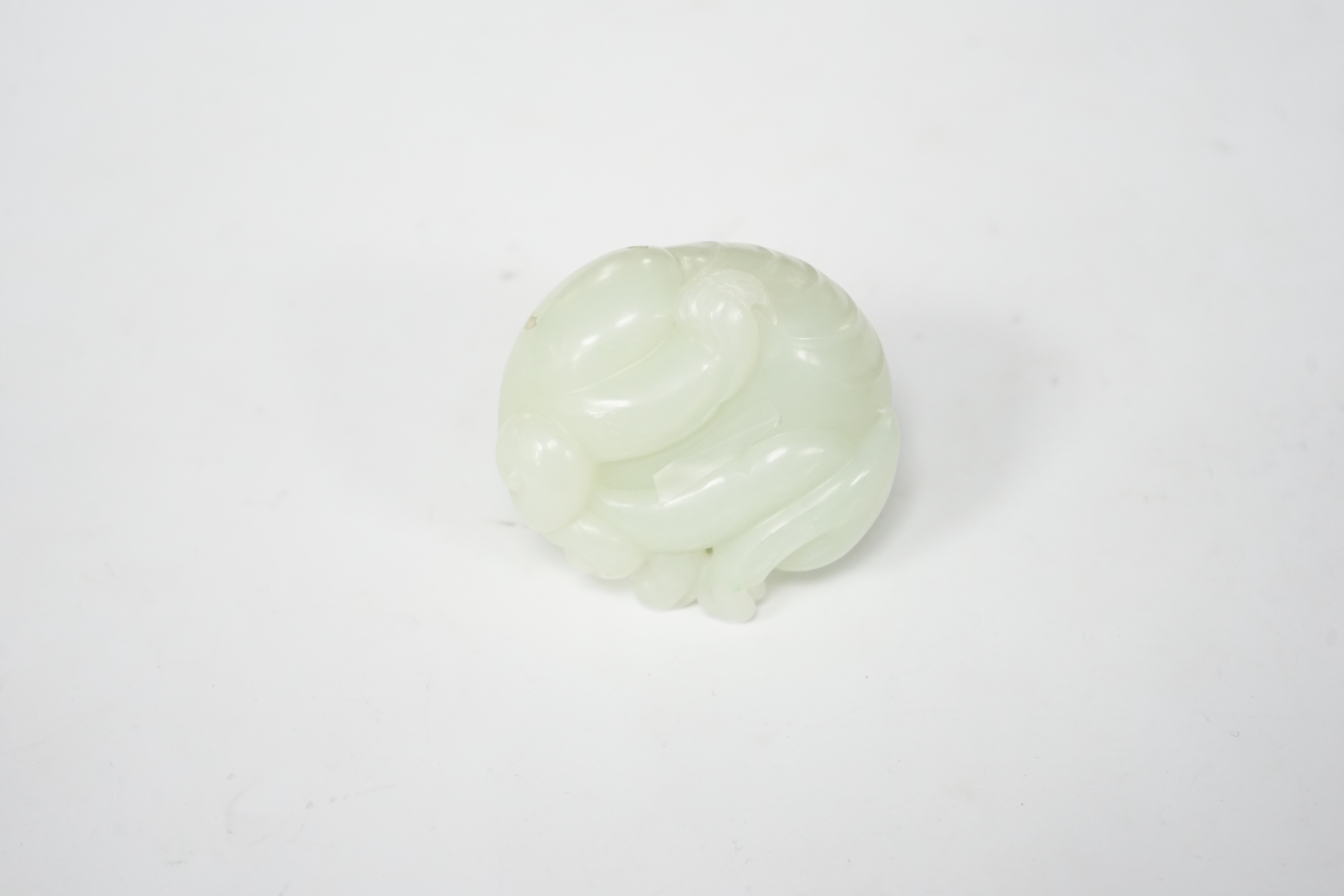 A Chinese celadon jade carving of a lion-dog, in recumbent pose, its crest with a russet inclusion, 5.3cm